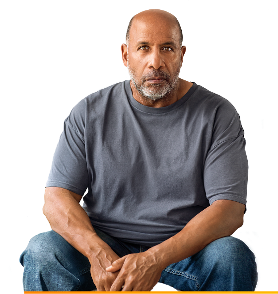 A male patient in a dark gray t-shirt sits with his forearms on his knees